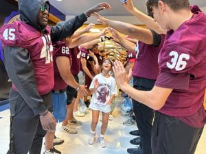 Picture of Round Rock high school football players creating a tunnel with their arms and Fern Bluff students running under it.
